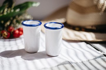 two white porcelain glasses, a hat, Lily of the valley bouquet, strawberries on a wooden table, sunlight on the terrace