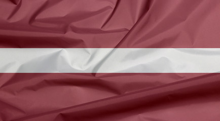 Fabric flag of Latvia. Crease of Latvian flag background, a carmine field bisected by a narrow...