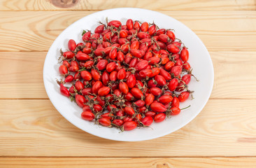 Dried red rose hips on white dish on wooden surface