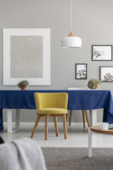 Yellow wooden chair at table with blue cloth in modern dining room interior with mockup. Real photo