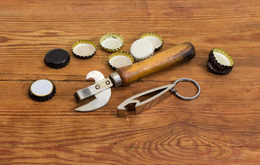 Two different bottle openers among of bottle caps on table
