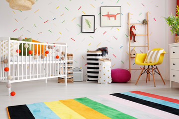 Colorful rug and yellow chair in child's room interior with cradle and posters on wallpaper. real...
