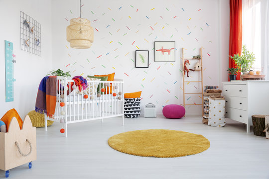 Fototapeta Orange round rug and posters in colorful kid's room interior with cradle and wooden crate. Real photo