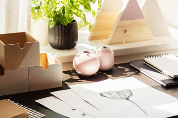 Close-up on desk with drawings and wooden boxes in workspace interior with plant. Real photo