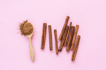 Cinnamon on pink background. Ground cinnamon and cinnamon sticks on pastel pink background, top view
