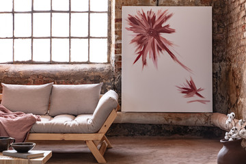 Poster next to window in industrial living room interior with grey wooden settee with blanket. Real...