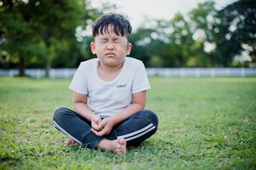 Asian children cute or kid boy sit for meditation with peace and relax in public park and wearing white dress with sunlight on white with space
