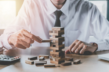 Hand of businessman pulling out or placing wood block on the tower in modern office. Risk and...