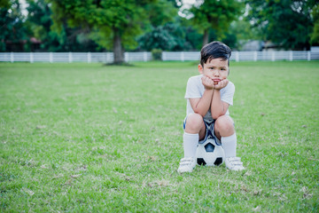 Little Asian child playing football and celebrating on grass.