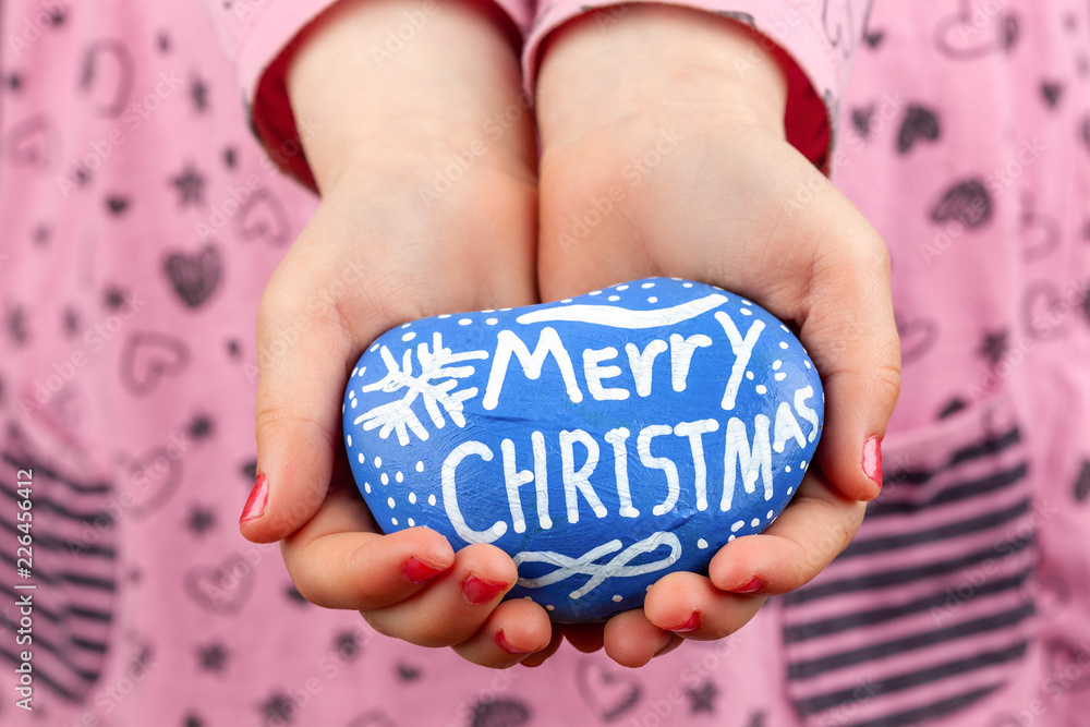 Wall mural child holding blue painted rock with merry christmas lettering closeup