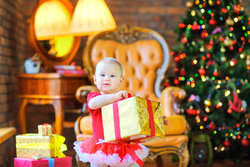 Obraz na płótnie Canvas little girl holding a gift by a red ribbon, against the background of a festive Christmas tree