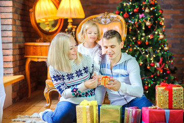 Fototapeta na wymiar happy family sitting on the floor near the Christmas tree congratulates and gives each other gifts