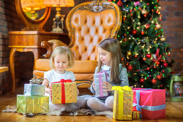 Fototapeta na wymiar two girls sitting on the floor near the Christmas tree give gifts