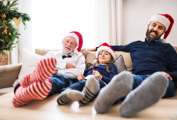 A small girl with father and grandfather sitting on a sofa at Christmas time.