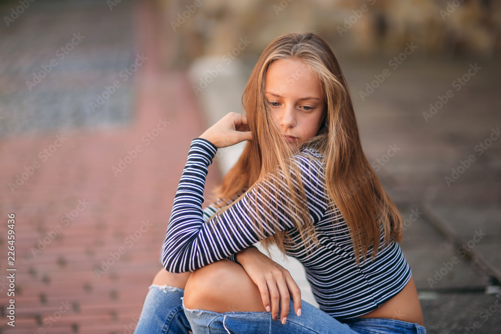 Wall mural young teenage poses to photographer. blonde girl in jeans and blouse