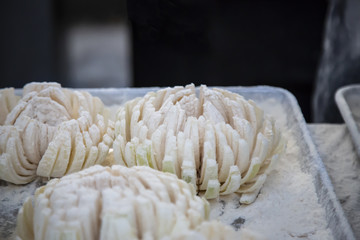Isolated close up view of floured  blooming onions on metal tray with out of focus backgrounds