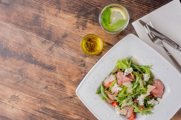 Fresh salad with roast beef, arugula, cherry tomatoes and Dor Blue cheese on a wooden background.