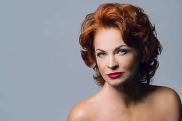 Closeup portrait of mature redhead woman with bright red lips, blue eyes. Female with evening...