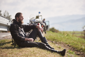 Athletic sportive motorcyclist in black leather clothing sitting at powerful motorbike on grassy...