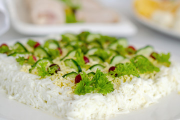 Mimosa salad garnished with sliced cucumbers and parsley sprigs. A traditional dish for banquets in Russian and Ukrainian cuisine. Selective focus.