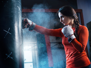 Young woman training punch boxing gloves for punching bag. Girl making Strong kick. CrossFit.