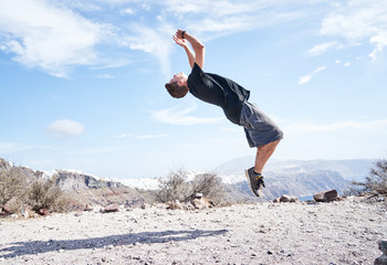 Mann macht Parkour und springt einen Salto vor der Küste Santorins 