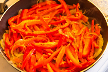 Pepper stew with onions in a pan close-up, top view