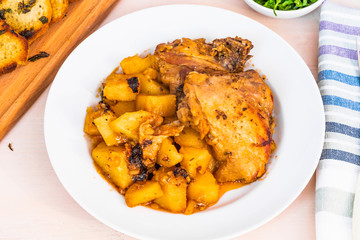 French food - chicken stew with potatoes in tomato sauce on a white plate with fried croutons, top view