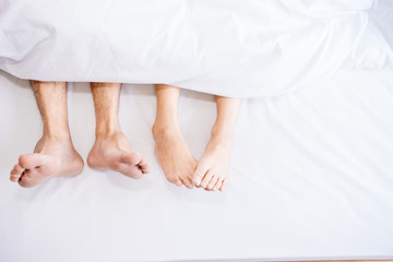 The feet or foot of couples sleeping on the bed and cover by the white blanket on a bright Sunday morning.