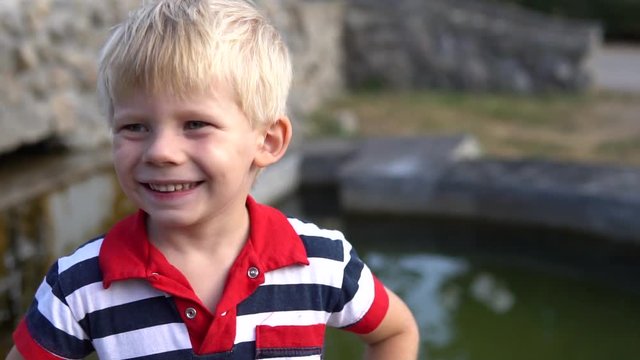 A little boy rejoices and smiles outdoors against the backdrop of a fountain. 3-4 years