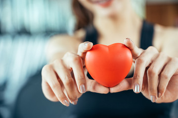 Asian sport woman holding red heart in fitness or gym center. Medical cadio heart strength training lifestyle. Pretty female sport girl workout exercise. Red massage ball in hand.