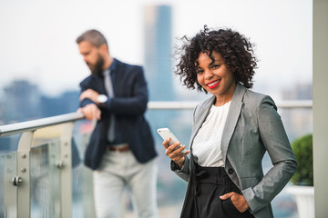 A portrait of a businesswoman with smartphone standing on a terrace.