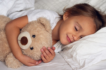 Portrait of a young girl (kid) sleeping in the bed with the teddy bear.