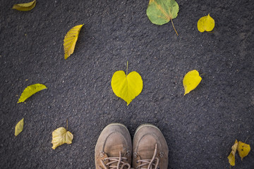 Autumn season, feet in shoes and heart shaped leaf on the ground
