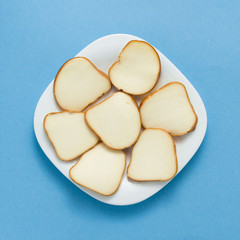 Slices and piece of cheese on plate on blue colored background, top view