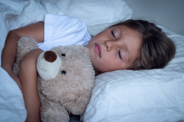 Portrait of a young girl (kid) sleeping in the bed with the teddy bear.