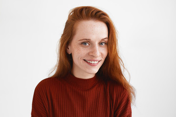 Horizontal shot of beautiful young freckled red haired female wearing stylish turtleneck looking at...