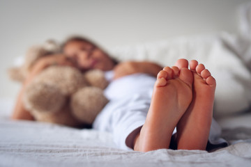 Close up of the feet of a young girl (kid) while she is sleeping on her bed with the teddy bear