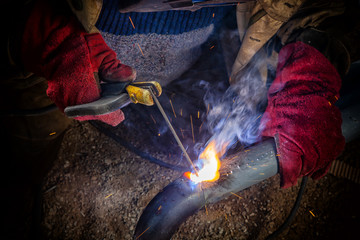 Close up welder weld metal pipe at construction site. A  builder in brown uniform, welding mask and...