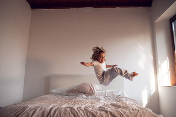 Portrait of a young girl (kid) while she is jumping on her parents bed. Concept: Happiness, freedom, family