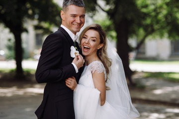 Groom in black tuxedo hugs tender stunning bride while they stand on the street of old European town