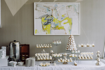 Luxury white wedding candy bar stands before a wall with modern art in the restaurant