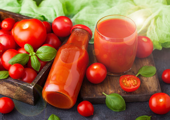 Bottle of fresh organic tomato juice with fresh raw tomatoes in box on stone kitchen background on black