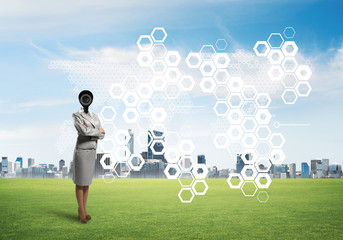Camera headed woman standing on green grass against modern cityscape