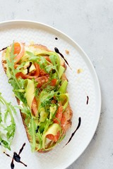 Brusctta with avocado, salmon, fresh leaves of arugula and balsamic. Breakfast with fresh organic greens, snacks, gravlax