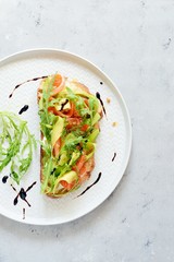 Brusctta with avocado, salmon, fresh leaves of arugula and balsamic. Breakfast with fresh organic greens, snacks, gravlax