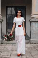 Portrait of charming brunette bride in white dress with red accessories