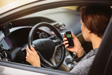 Young millennial woman using breath alcohol analyzer in the car. Closeup with selective focus. Girl taking alcohol test with breathalyzer.