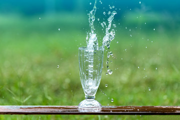 Drink water pouring in to glass over sunlight and natural green background.Select focus blurred background.Fresh Clean water splash.