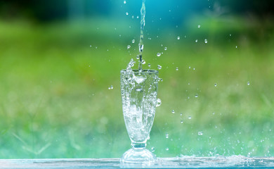 Drink water pouring in to glass over sunlight and natural green background.Select focus blurred background.Fresh Clean water splash.